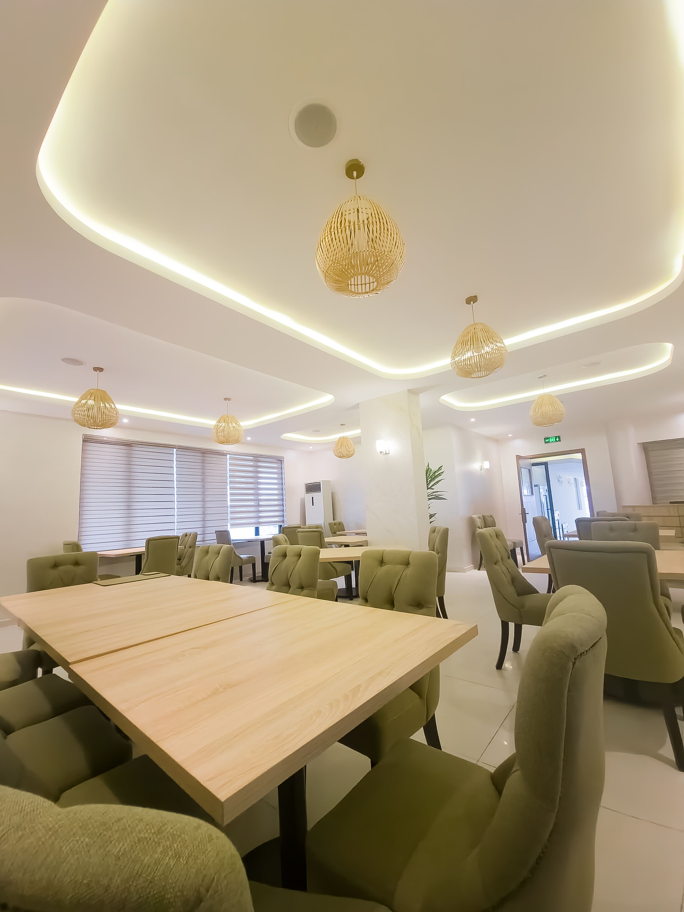 A modern conference room with a large table, green upholstered chairs, and pendant lighting.