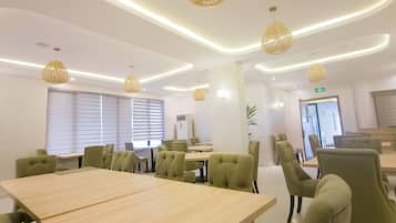 A modern conference room with a large table, green upholstered chairs, and pendant lighting.