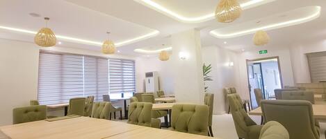 A modern conference room with a large table, green upholstered chairs, and pendant lighting.