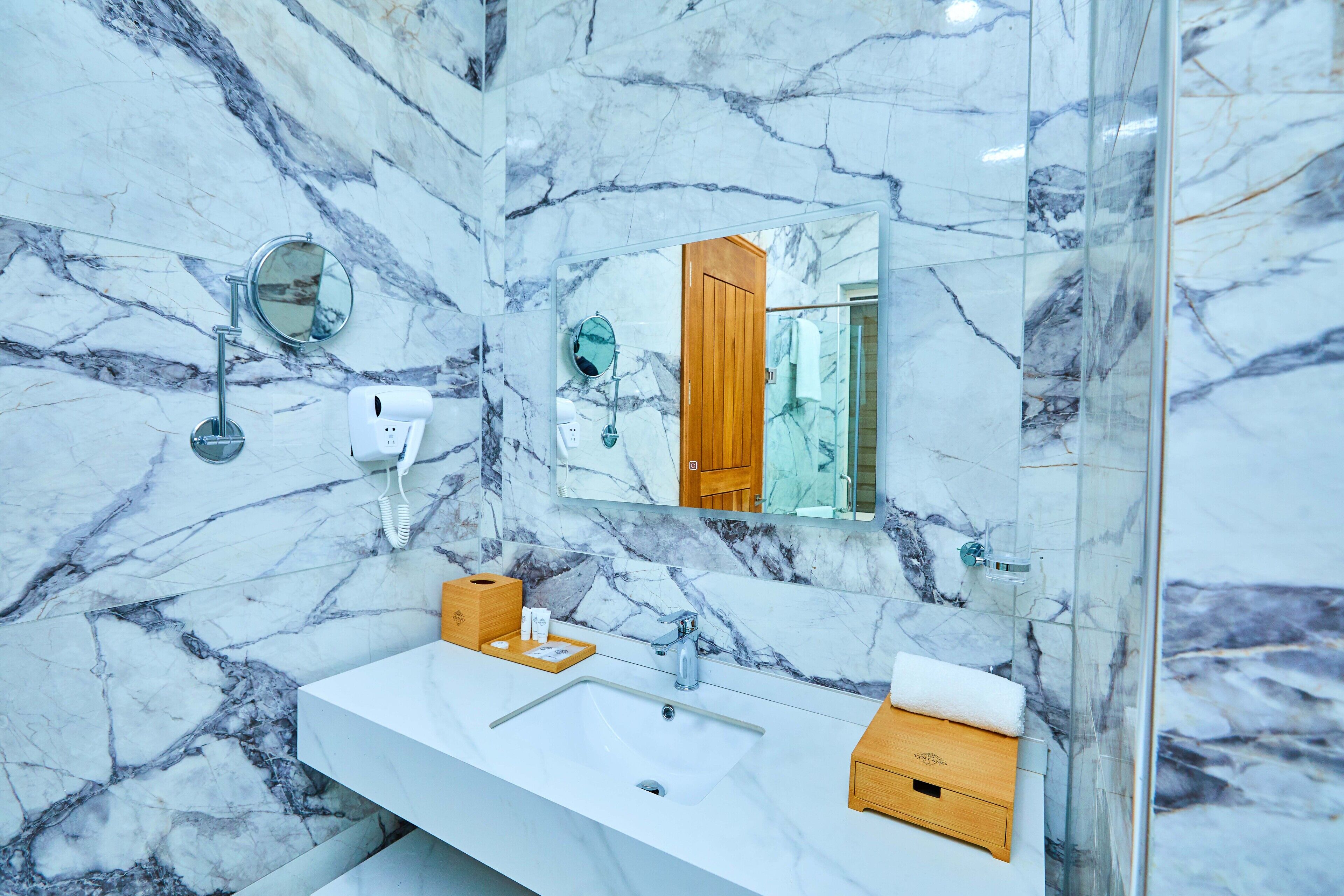 A bathroom with a marble wall, a large mirror, a sink, and a shower area.