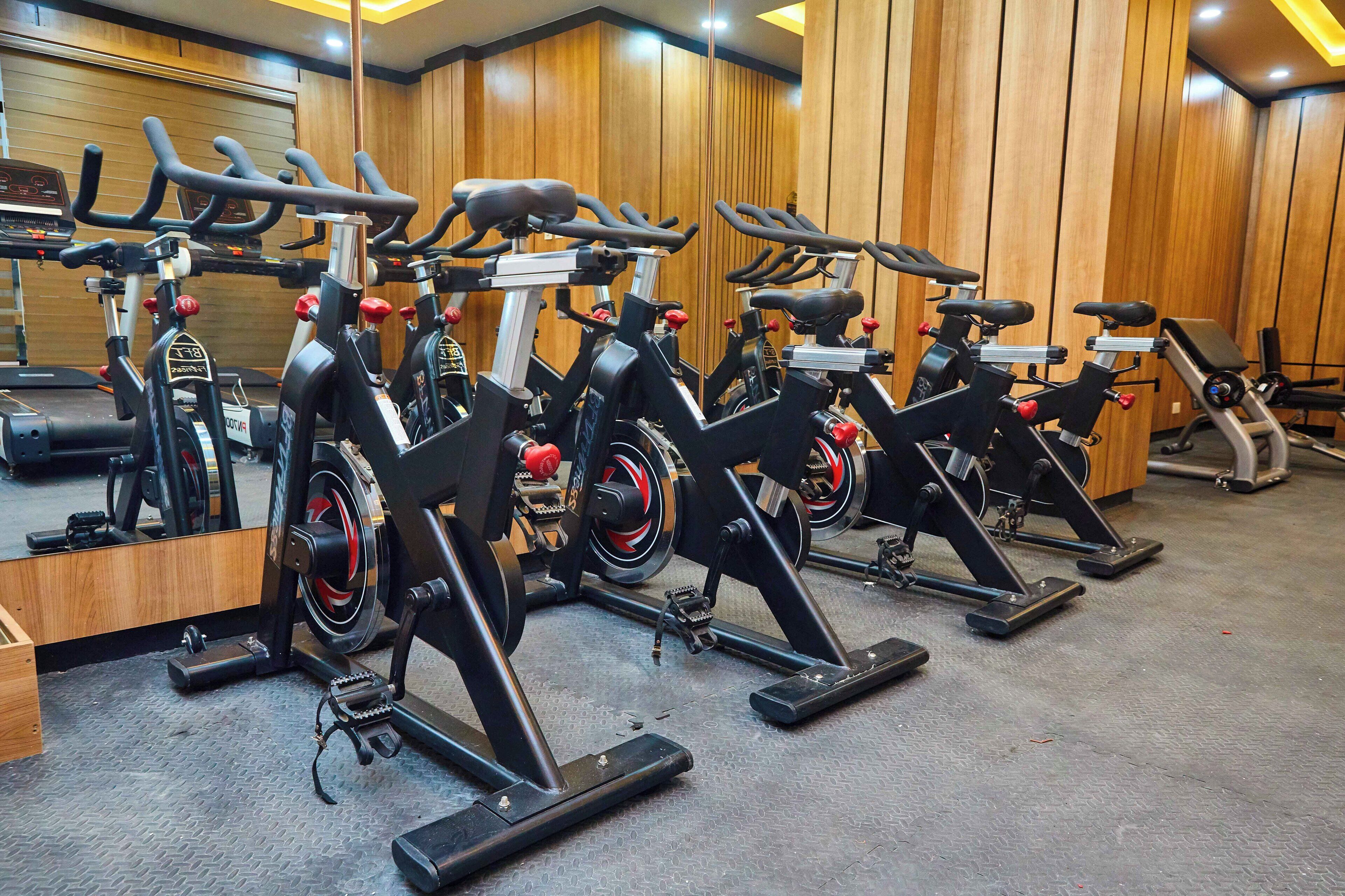 A row of stationary bikes in a gym with wooden walls and a mirrored wall.