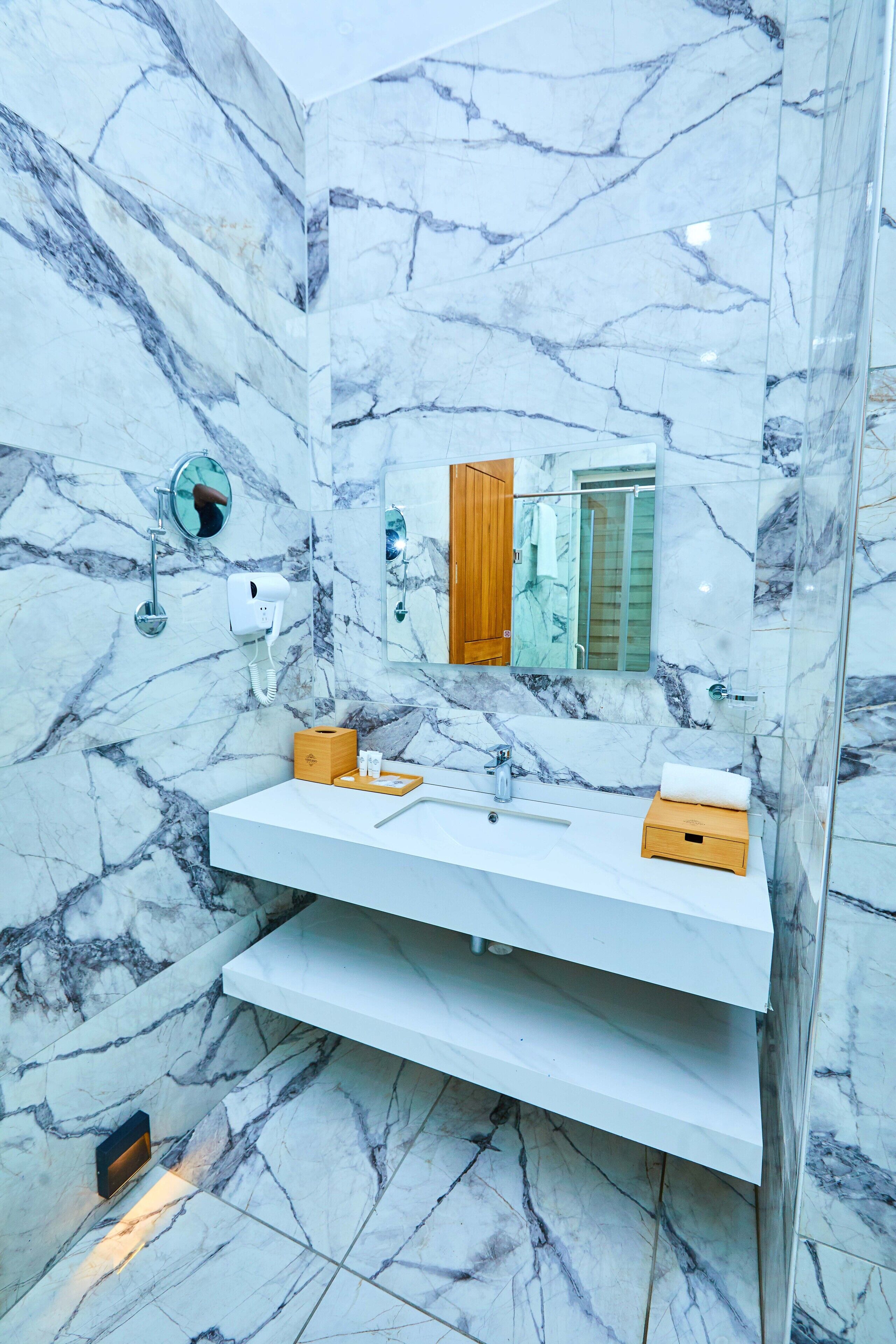 A bathroom with a marble wall, a white sink, a wooden box, and a mirror.