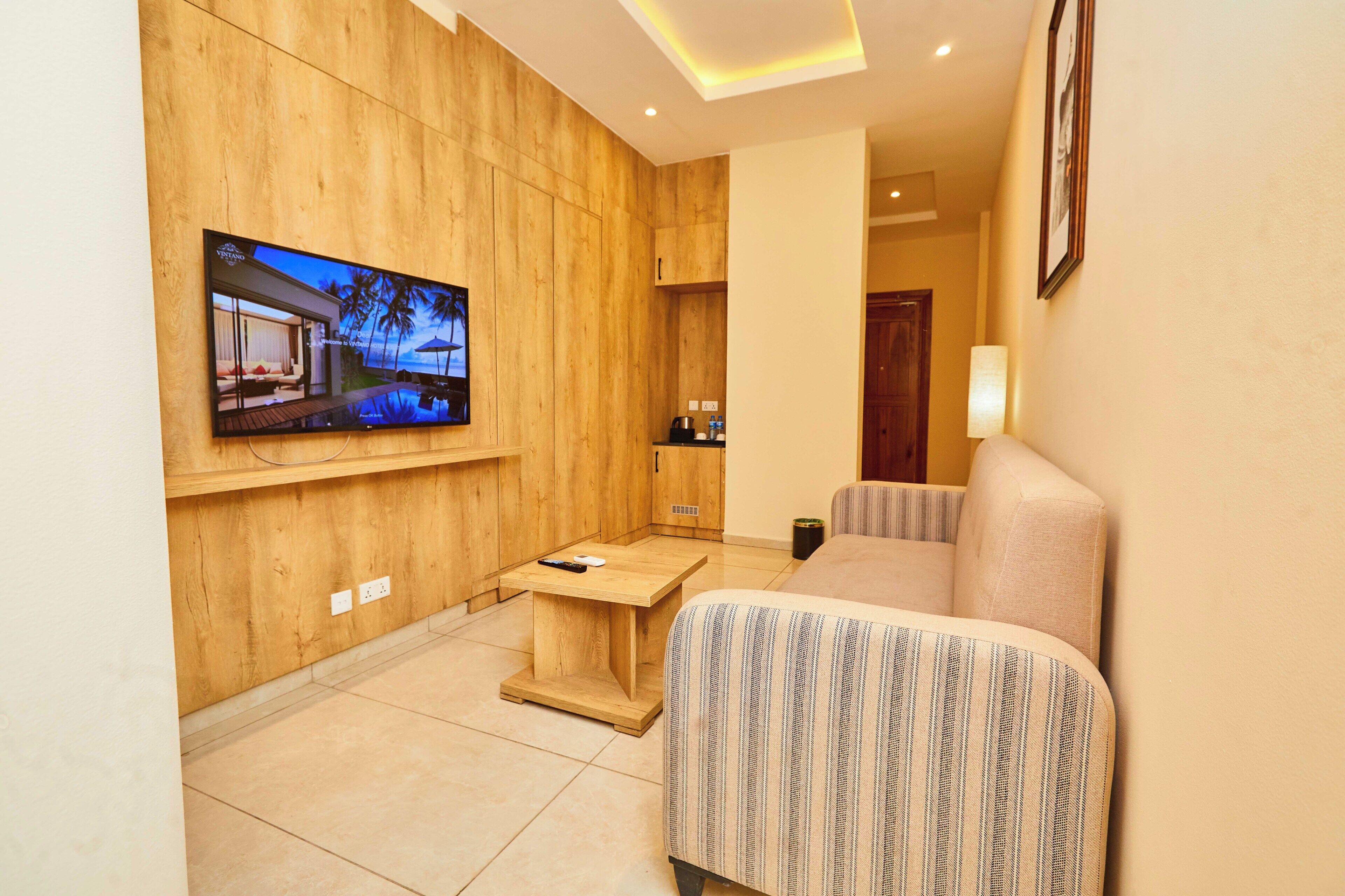 A modern living room with a flat-screen TV mounted on a wooden wall, a small wooden side table, a sofa, and a lamp.