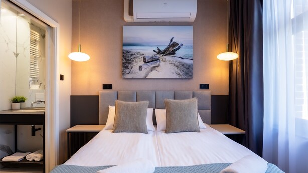 A hotel room with a large bed, two bedside tables, a nightstand, a wall-mounted air conditioner, and a painting of a beach scene. - Motto Gdańsk (Gdansk)