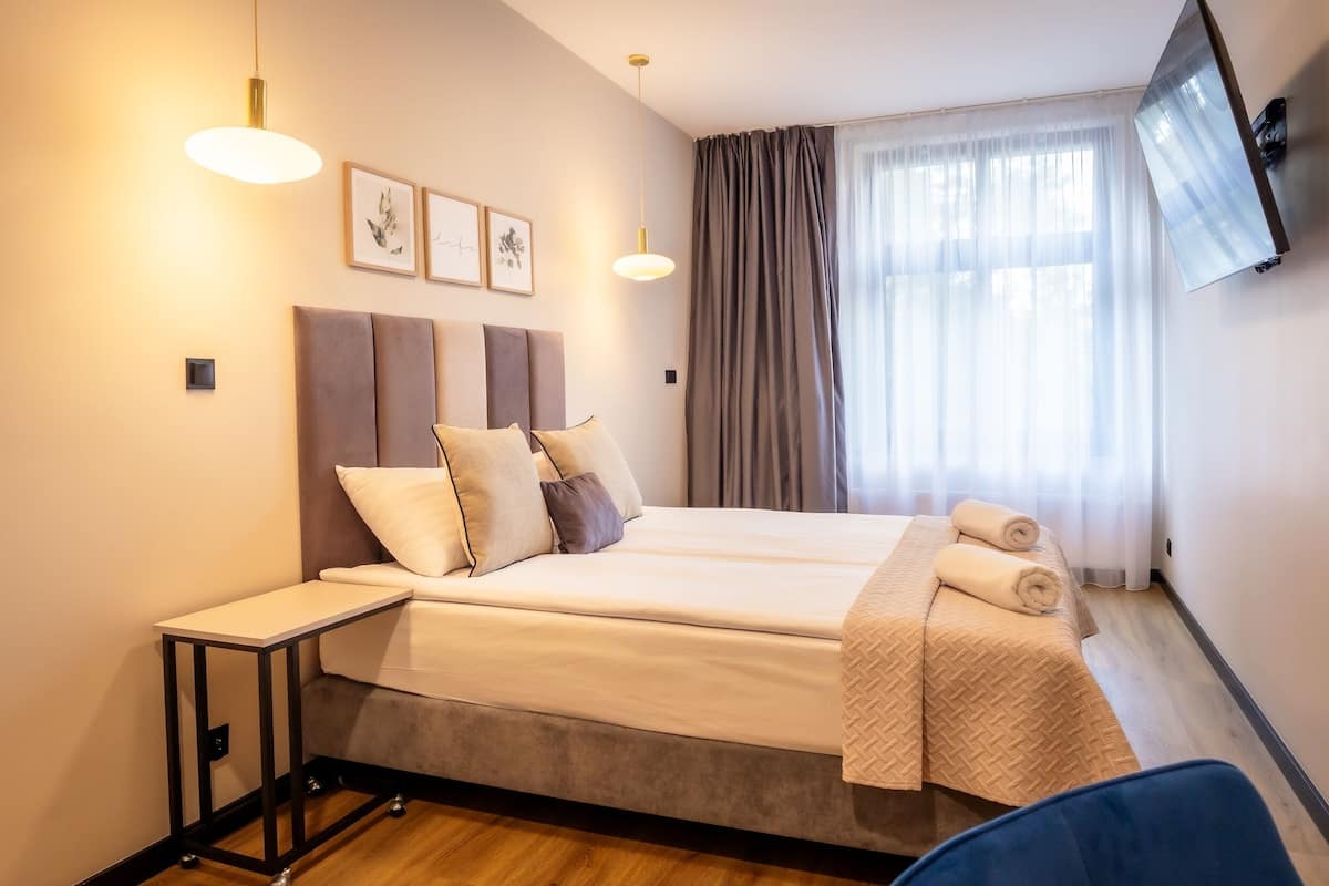 A modern hotel room with a large bed, bedside tables, a flat-screen TV, and artwork on the wall.