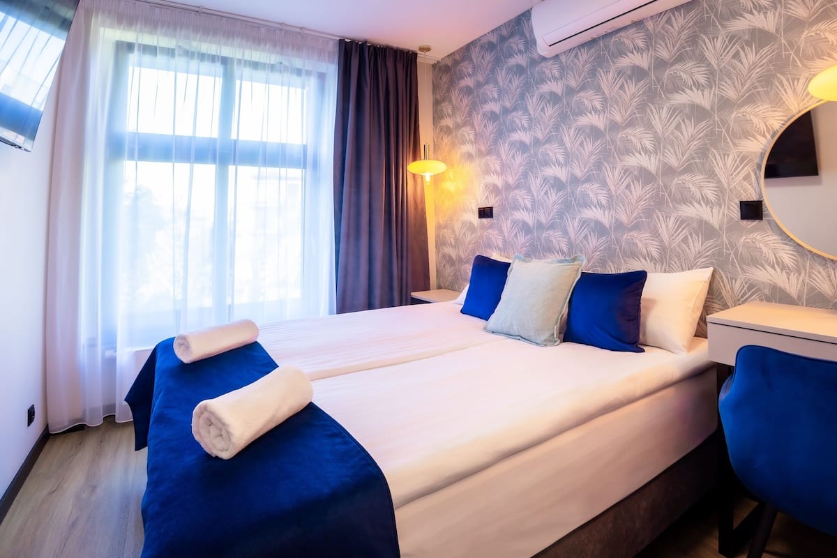 A hotel room with a large bed, two pillows, a bedside table, a lamp, and a mirror.