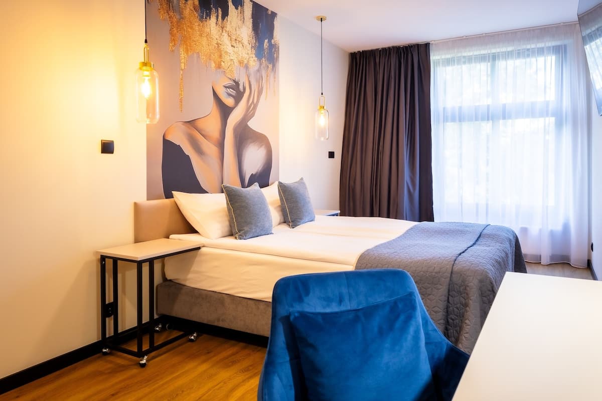 A modern hotel room with a large bed, a small table, a chair, and a wall mural.