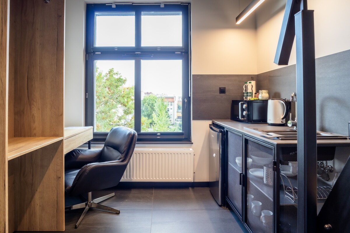 A compact kitchenette with a window, a chair, and a built-in refrigerator.
