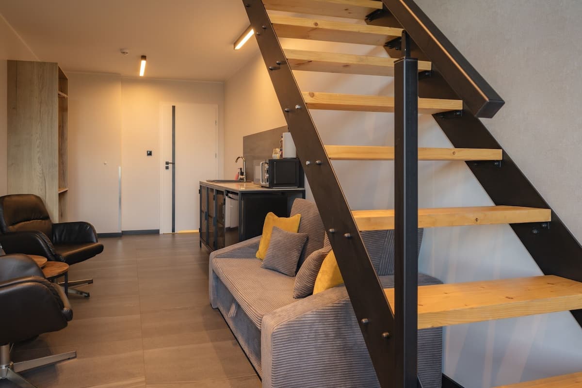 A modern interior with a wooden staircase, a sofa with cushions, leather chairs, and a small table with a coffee machine.