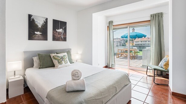 A hotel room with a bed, a nightstand, a lamp, two framed pictures on the wall, and a view of the outside through a large window. - GuestReady - Portrait with a view (Porto)