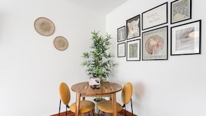 A dining area with a round wooden table, two yellow chairs, a potted plant, and framed artwork on the wall. - GuestReady - Portrait with a view (Porto)