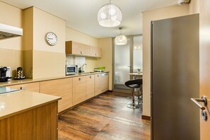 Eine moderne Küche mit Holzausstattung, einem Edelstahlkühlschrank, einer Mikrowelle und einer Kaffeemaschine.