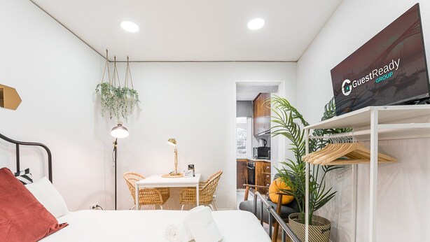 A modern hotel room with a bed, a desk with a chair, a hanging plant, and a wardrobe with a mirror. - GuestReady - Road to Revolution (Porto)