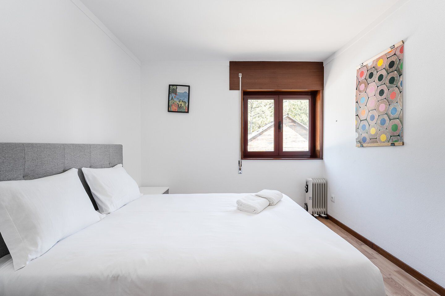 Ein Schlafzimmer mit Bett, Fenster, Heizkörper und einem Wandbild.