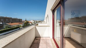 A balcony with a view of a residential street, a clear sky, and a building with a red frame window.