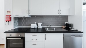 A modern kitchen with white cabinets, a black countertop, a stainless steel sink, a toaster, a kettle, and a coffee maker.