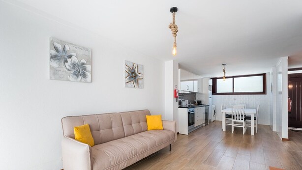 A modern living room with a beige sofa, a dining table, and a kitchen in the background.