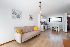 A modern living room with a beige sofa, a dining table, and a kitchen in the background.