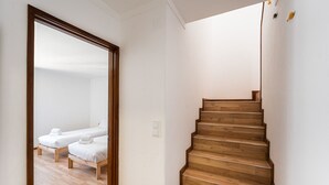 A staircase with wooden steps leading to a bedroom with two beds.