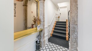 Un escalier avec des marches recouvertes de moquette noire, une étagère en verre ornée d’objets décoratifs et un miroir avec un cadre doré.