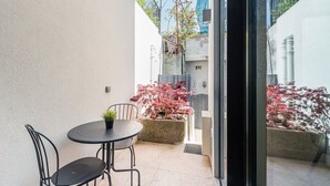 Un petit espace extérieur aménagé avec une table et deux chaises, un pot de fleurs et une vue sur un bâtiment aux feuillages rouges.