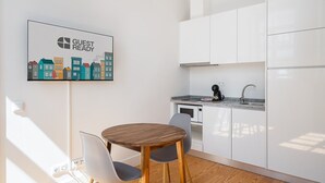 Une cuisine moderne avec des meubles blancs, une table à manger en bois accompagnée de deux chaises, une machine à café et un four à micro-ondes.