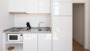Une cuisine compacte avec des meubles blancs, un plan de travail en granit, un four à micro-ondes encastré et une machine à café noire.