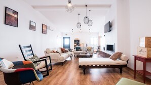 Un salón espacioso con sofá, sillón y otoman, suelo de madera y televisor montado en la pared.