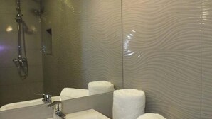 Un baño moderno con un espejo grande, un lavamanos y una ducha.