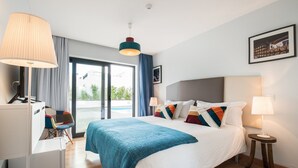 Una habitación de hotel moderna con una cama grande, un escritorio y una silla. Cuenta con una ventana con cortinas, una lámpara en el techo y un cuadro en la pared.