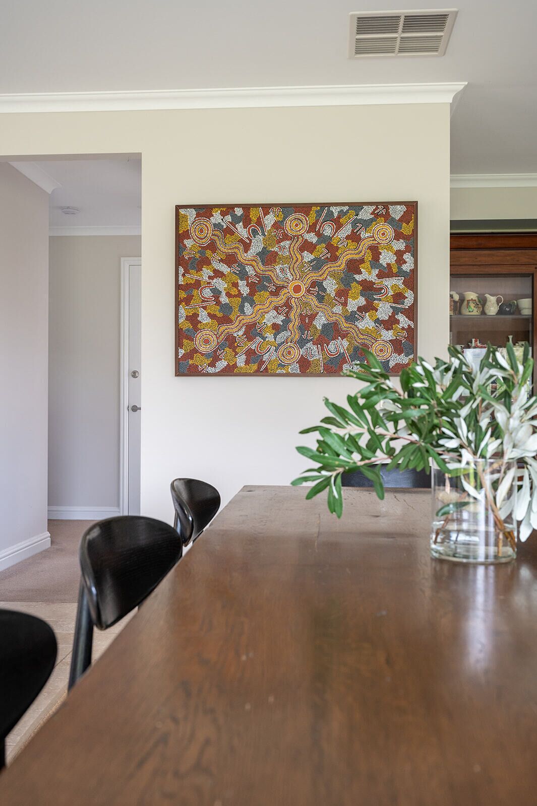 A dining area with a wooden table, black chairs, a colorful abstract painting on the wall, and a potted plant.