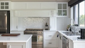 A modern kitchen with white cabinetry, a stainless steel refrigerator, a built-in oven, and a large island with a cutting board. - Bundjil Beach House I Walk to beach (Bass Coast)