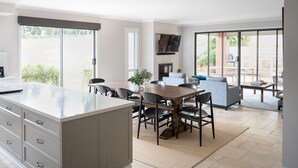 A modern kitchen with a dining area, a TV mounted above the fireplace, and a patio with outdoor seating. - Bundjil Beach House I Walk to beach (Bass Coast)