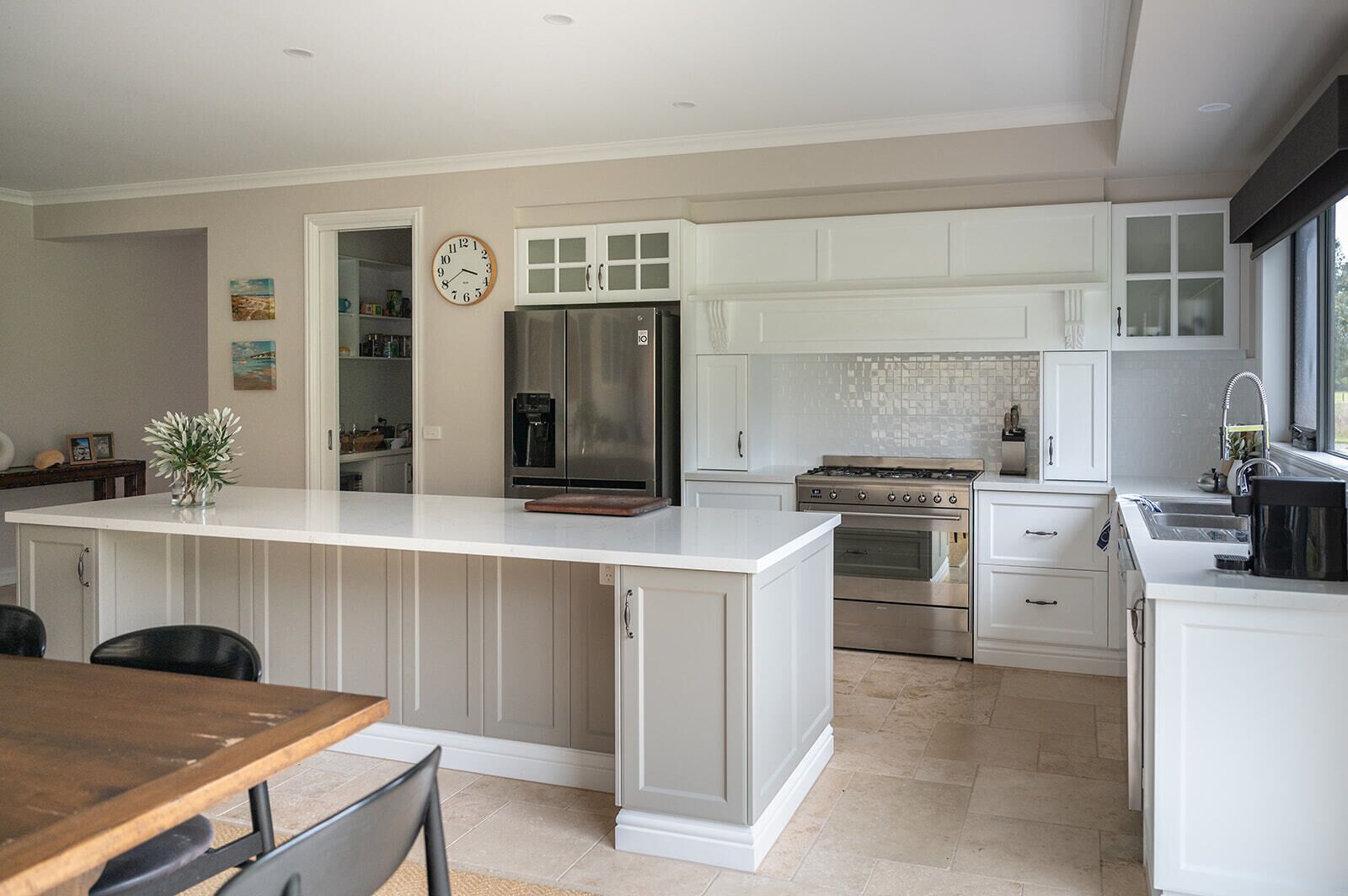 Een moderne keuken met witte kastjes, een centraal eiland, roestvrijstalen apparatuur, en een eethoek met een houten tafel en stoelen.