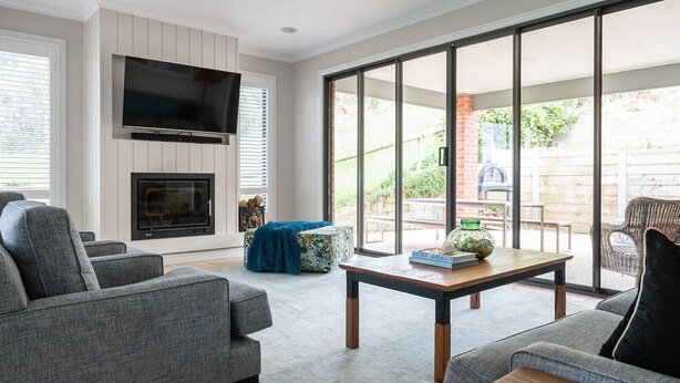 A living room with grey sofas, a flat-screen TV, a fireplace, and a large sliding glass door leading to an outdoor patio. - Bundjil Beach House I Walk to beach (Bass Coast)