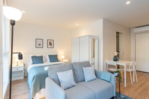 A modern hotel room with a bed, a grey sofa, a small table with chairs, a desk, and a mirror. - GuestReady - A peaceful city refuge (Porto)