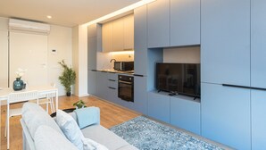 A modern kitchen with built-in appliances, a dining area with a white table and chairs, and a living area with a sofa and a TV mounted on the wall. - GuestReady - A peaceful city refuge (Porto)
