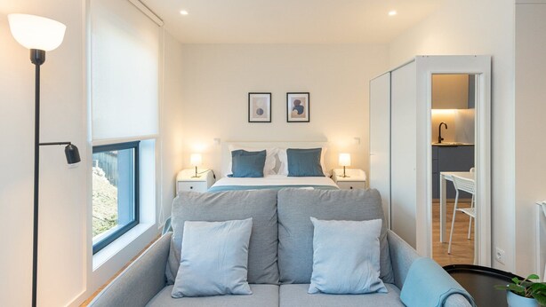 A modern hotel room with a bed, two bedside tables, a sofa, and a view of the outside. - GuestReady - A peaceful city refuge (Porto)