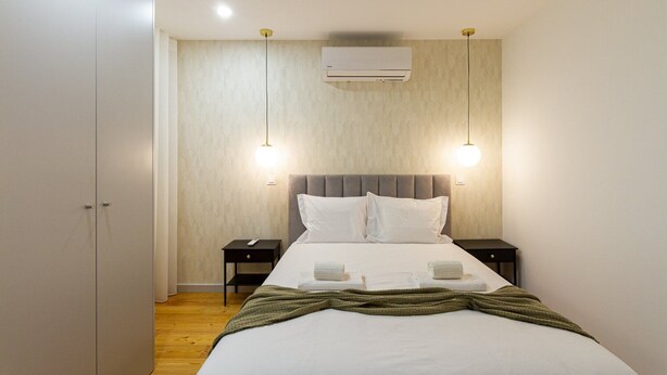 Een moderne slaapkamer met een bed, twee nachtkastjes, een airconditioner en hanglampen.