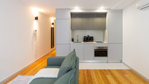 Een ruimtelijk ingerichte leefruimte met een kitchenette, een bank en een houten vloer.