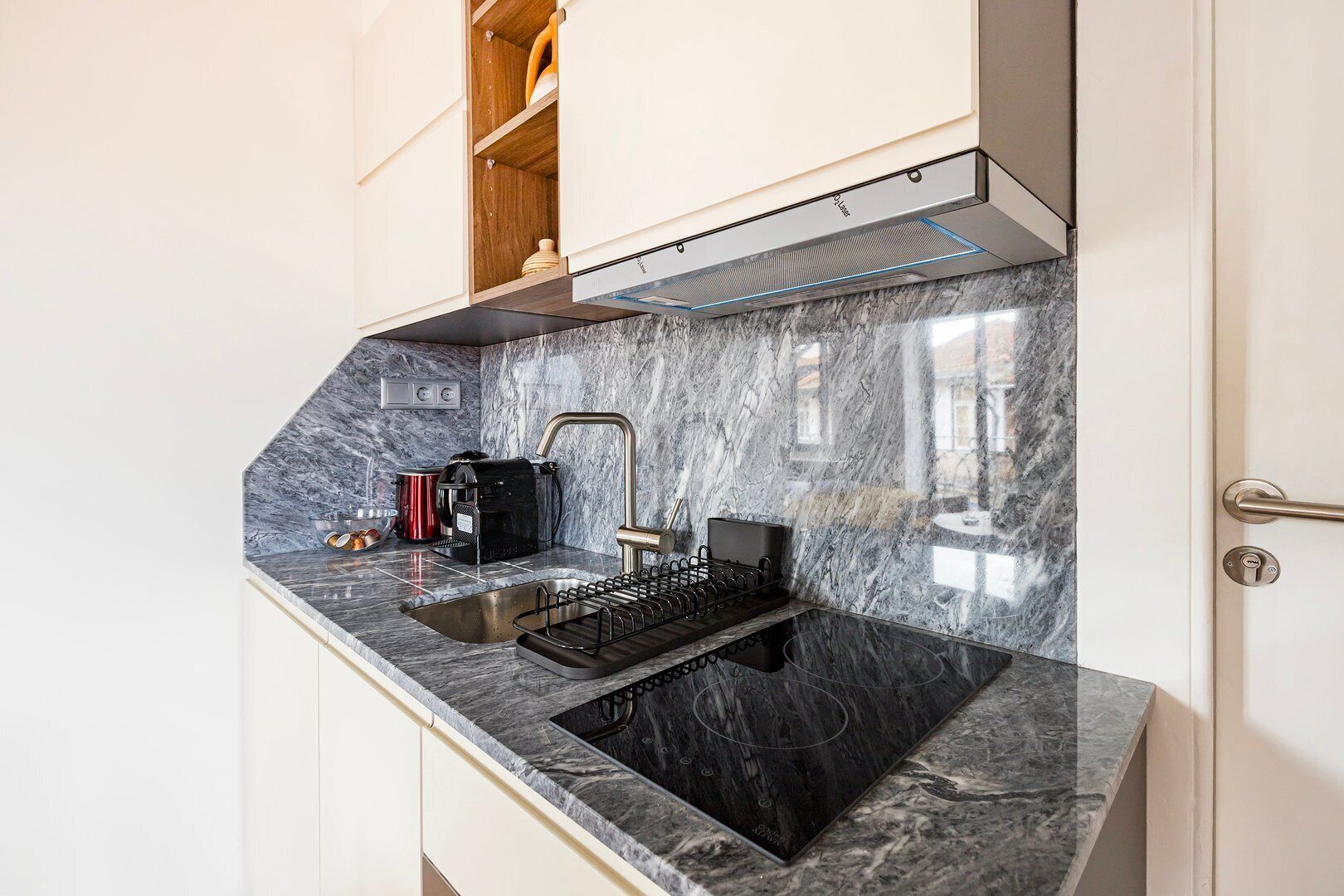 A modern kitchen with a marble countertop, a built-in oven, and a coffee machine.
