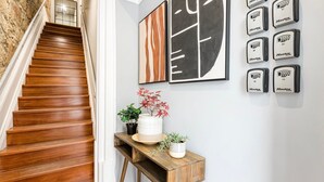 A wooden staircase leading to a landing with a white wall. On the landing, there are two potted plants and a small wooden table. - GuestReady - Caldeireiros Building (Porto)