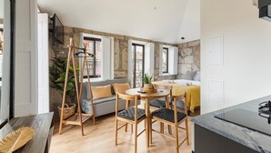 A compact living space with a sofa, dining table, and chairs, a bed with a yellow blanket, and a stone wall. - GuestReady - Caldeireiros Building (Porto)
