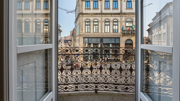 A view through a window with ornate iron railings, a building with classical architecture, and a clear sky. - GuestReady - RNB Code Violet (Porto)