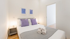 A bedroom with a bed, two pillows, a bedside table, a lamp, and two wall art pieces. - GuestReady - RNB Code Violet (Porto)