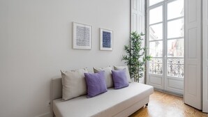 A modern living room with a beige sofa, two framed artworks, and a large window with a view of buildings. - GuestReady - RNB Code Violet (Porto)