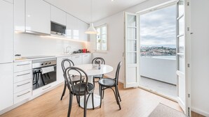Una cocina moderna con armarios blancos, horno empotrado y comedor con mesa redonda y cuatro sillas.