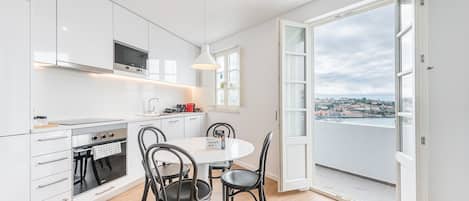 A modern kitchen with white cabinets, a built-in oven, and a dining area with a round table and four chairs.