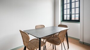 A dining area with a rectangular table and four wicker chairs, a window with a view, and a light-colored floor. - GuestReady - A brilliant stay near Ribeira (Porto)