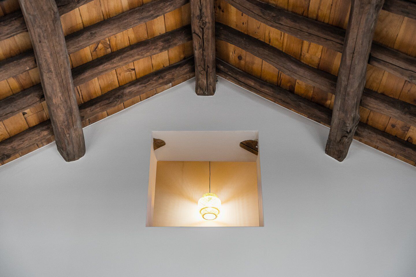 Ein Zimmer mit schräg verlaufender Decke, Holzbalken und einer hängenden Leuchte.